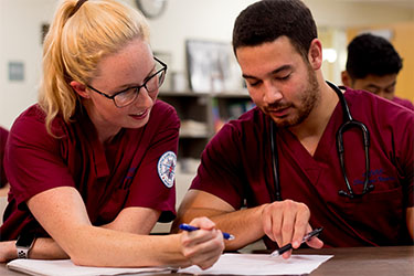 two nursing students in red scrubs studying together