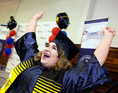 Student in graduation apparel raising arms in the air and smiling.