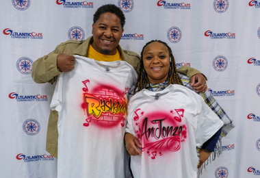 Two people posing for picture holding decorative t-shirts